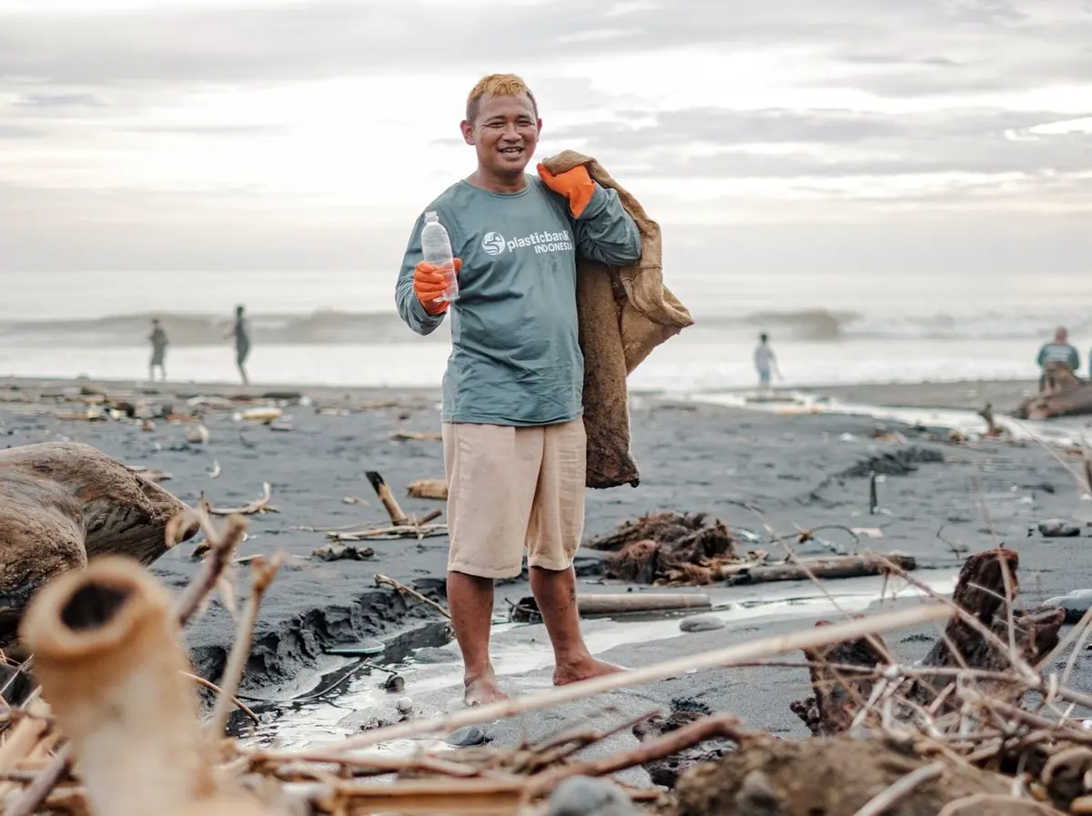 A collector holding up a plastic bottle on a beach strewn with washed-up debris
